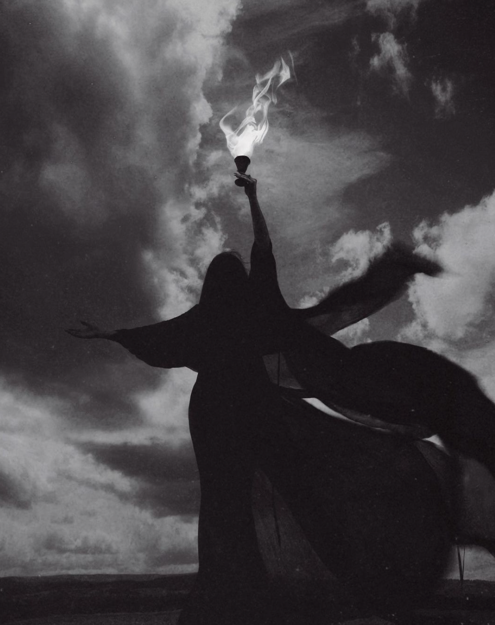black and white image of a woman holding a flame baring torch up into the stormy cloudy sky.