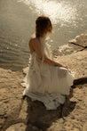 Woman in a white dress sitting by a body of water